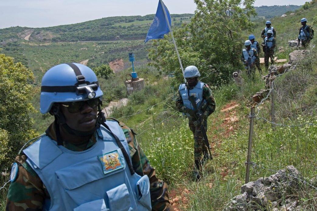 UN Peacekeepers trek through a field.