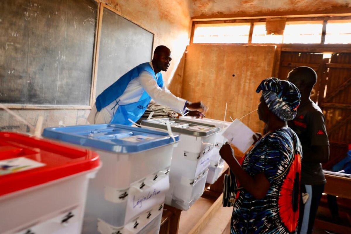 Un agent électoral aide des électeurs à déposer leurs bulletins.